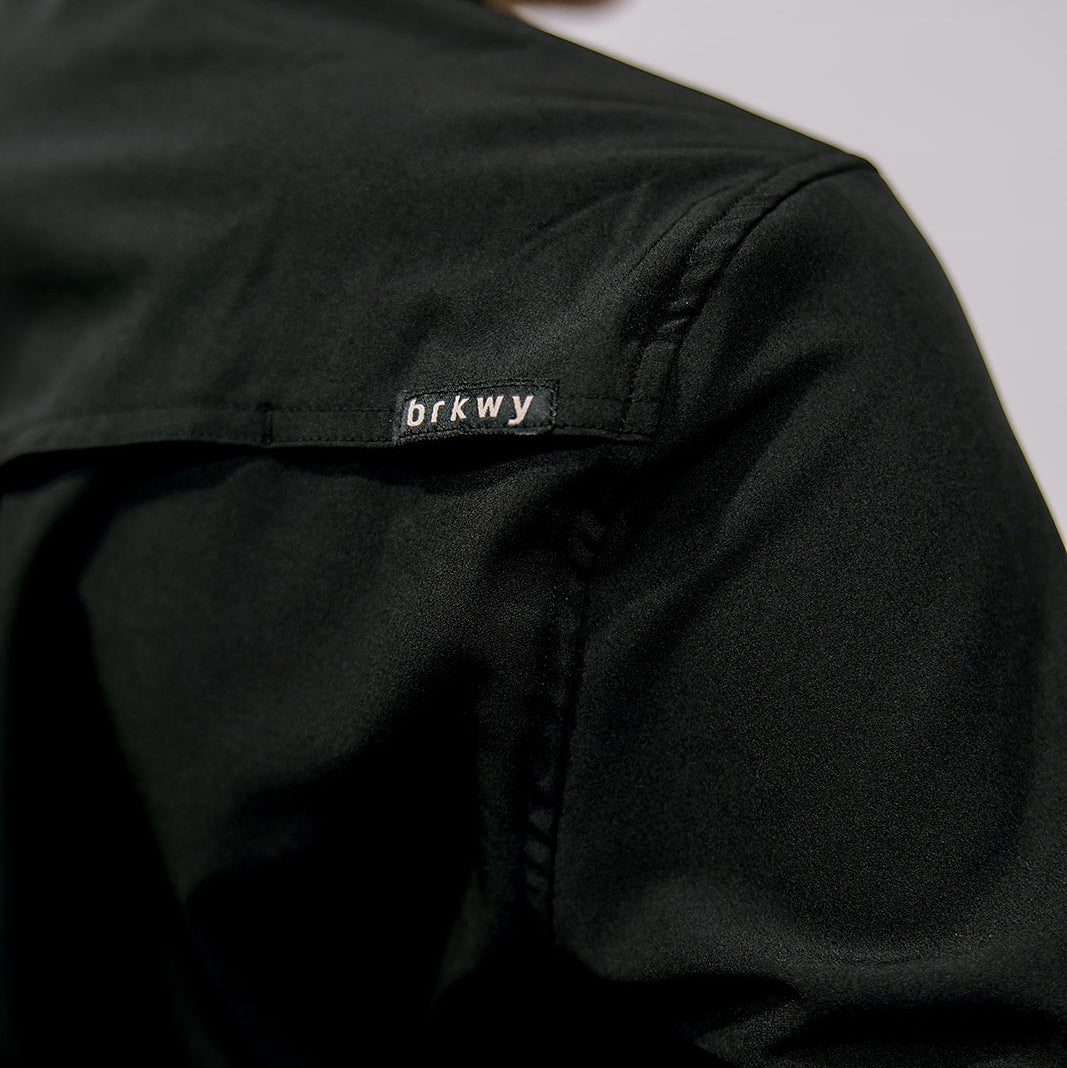 Black shirt  with a brand label on the sleeve against a neutral background