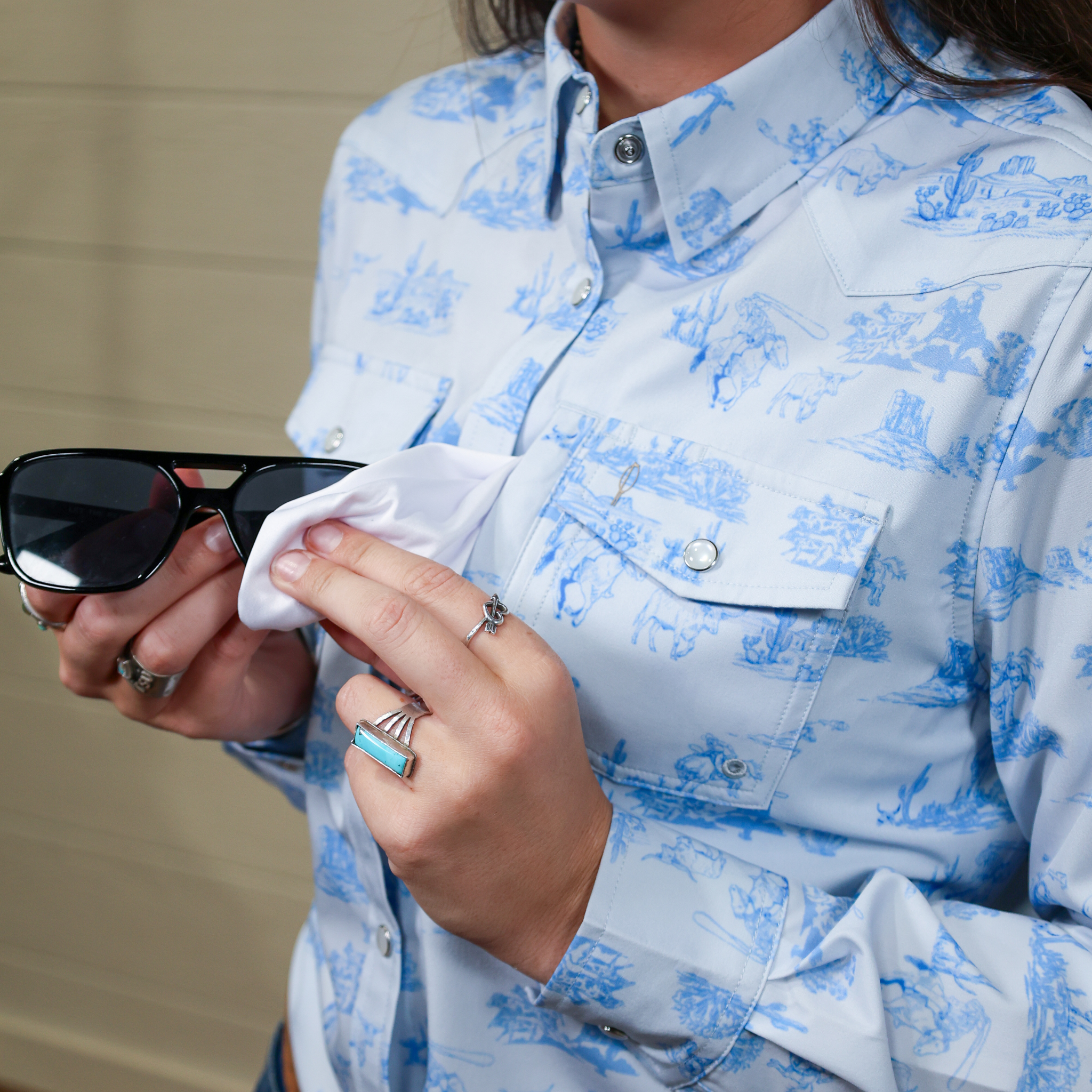 Person wearing a blue and white patterned shirt holding sunglasses.