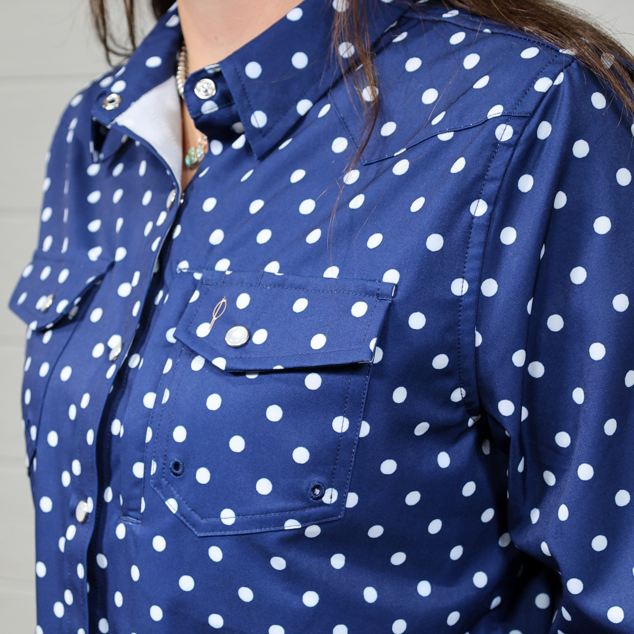 Close-up of a blue shirt with white polka dots on a neutral background. side facing.