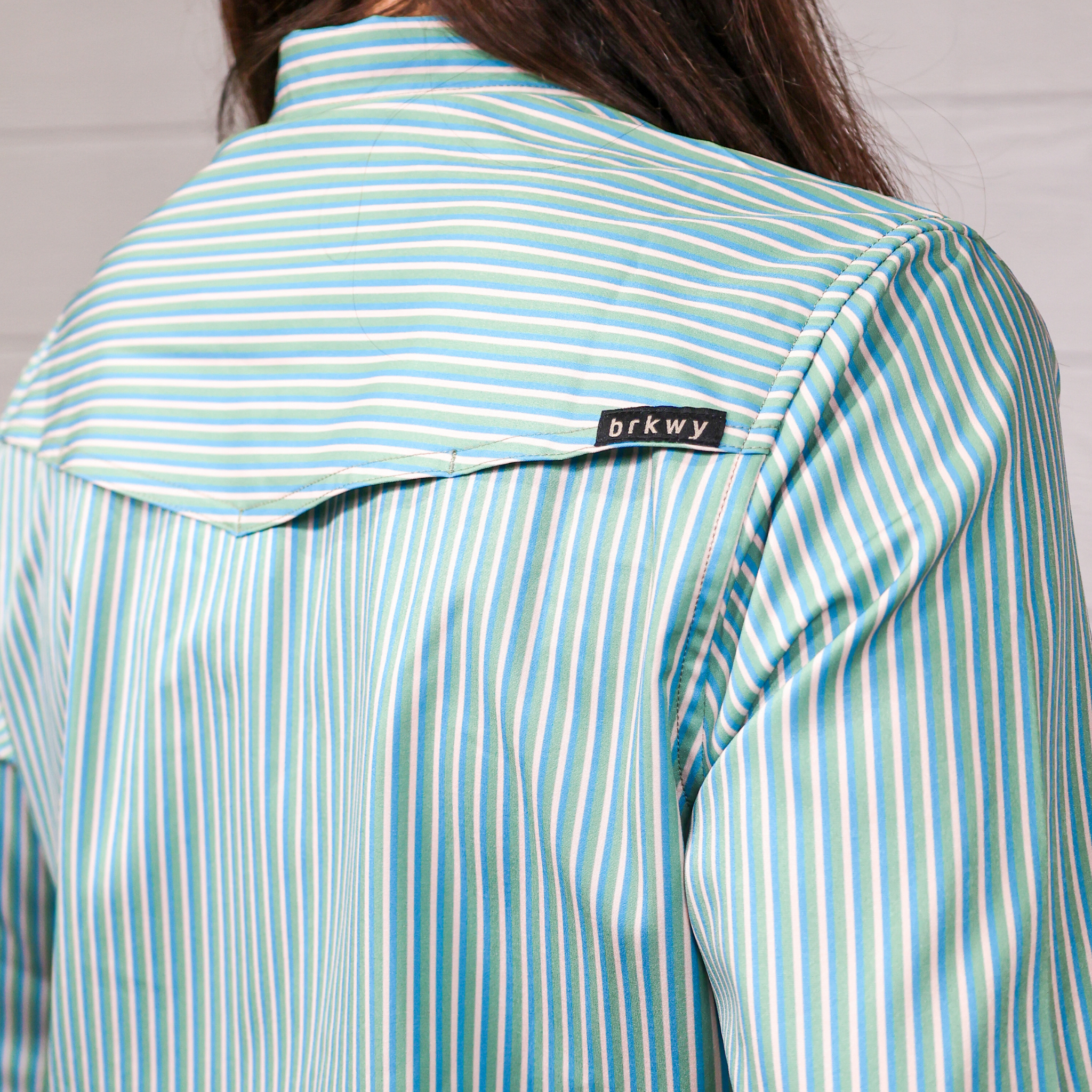 Close-up of a person wearing a light blue and white striped shirt with 'brkwy' label on white background. 