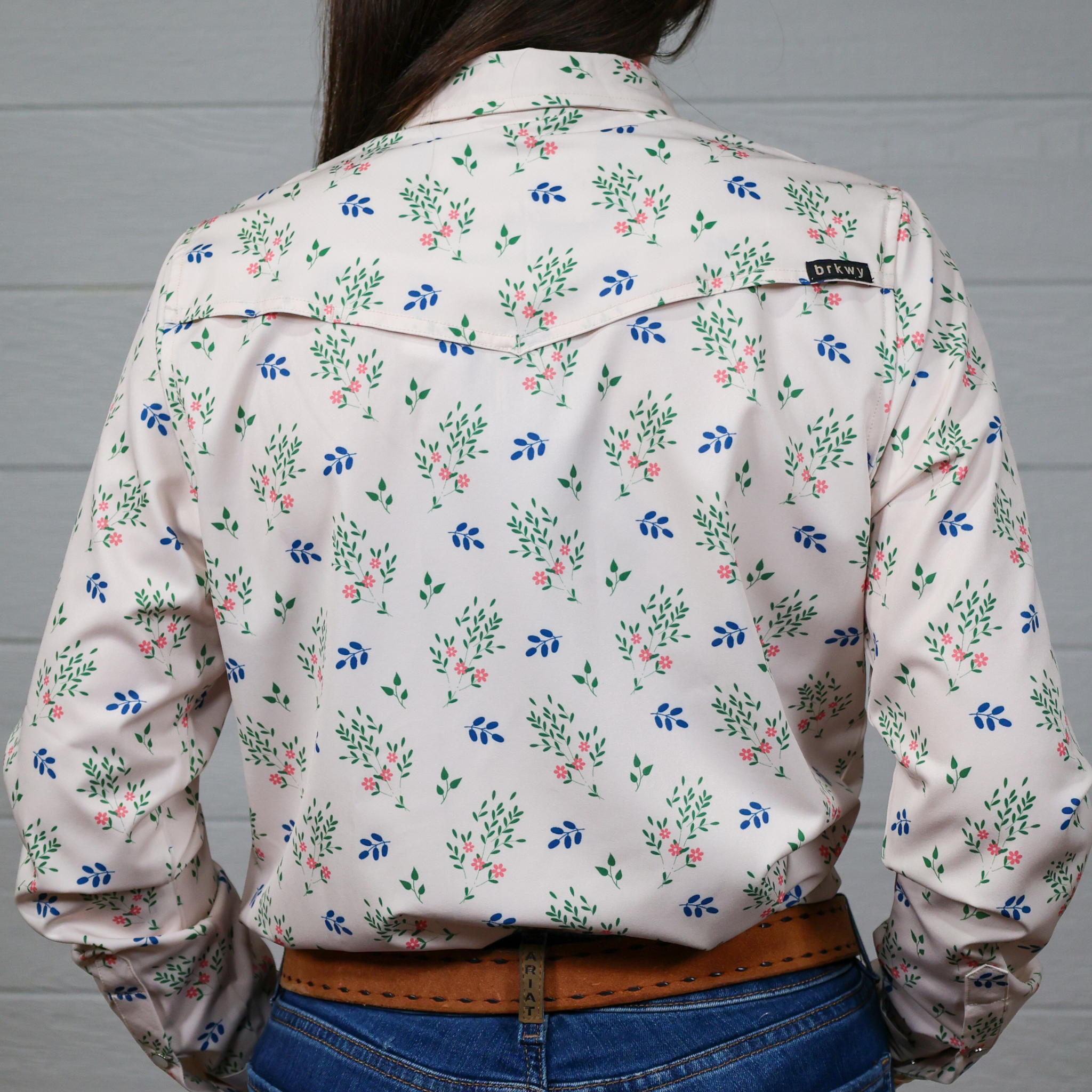 Person wearing a floral-patterned shirt with a visible brand logo against a white background. back facing