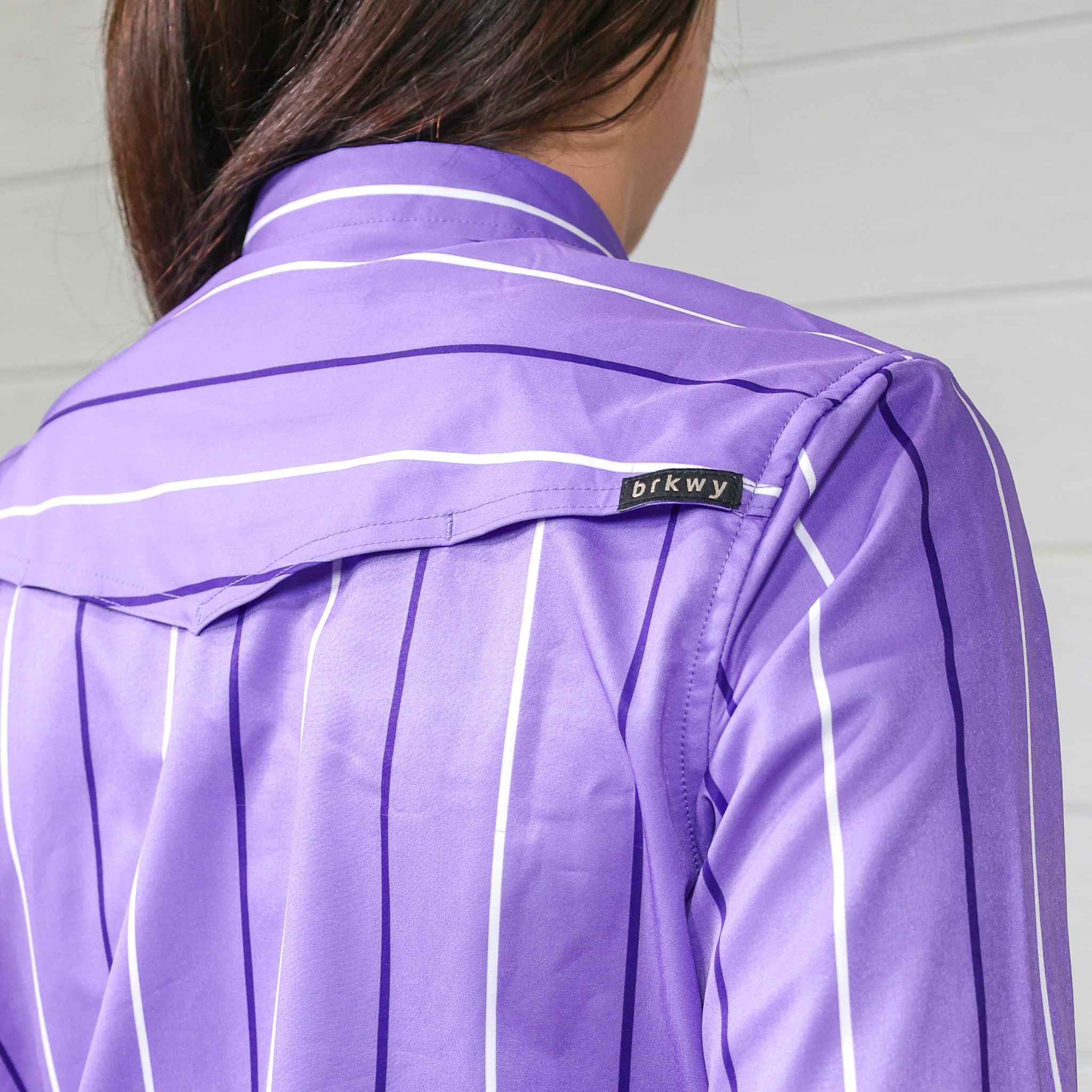 Purple women's button down with white stripes and a brand label on a neutral background