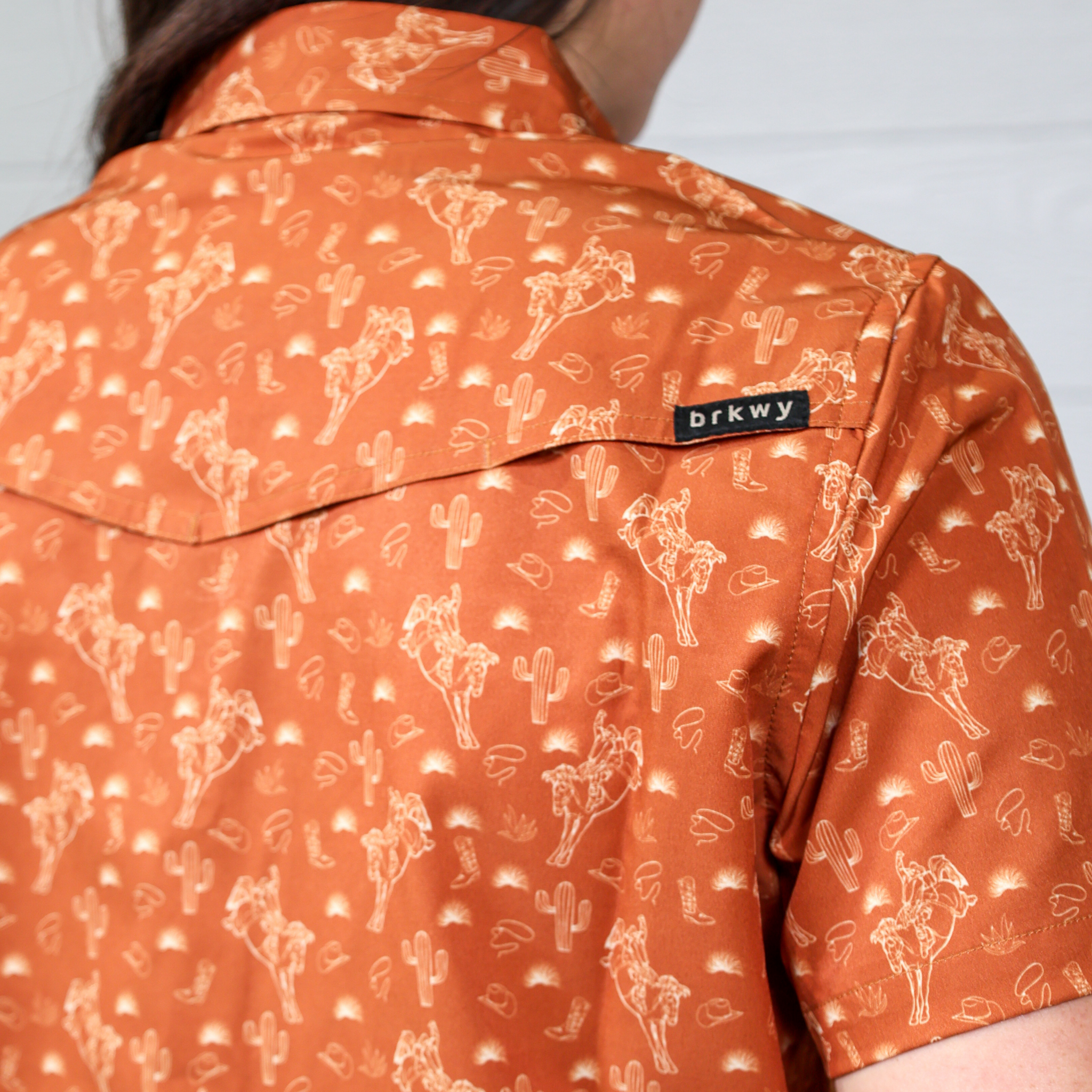 Orange shirt with white patterns and 'brkwy' brand label on a plain white background. Back facing.