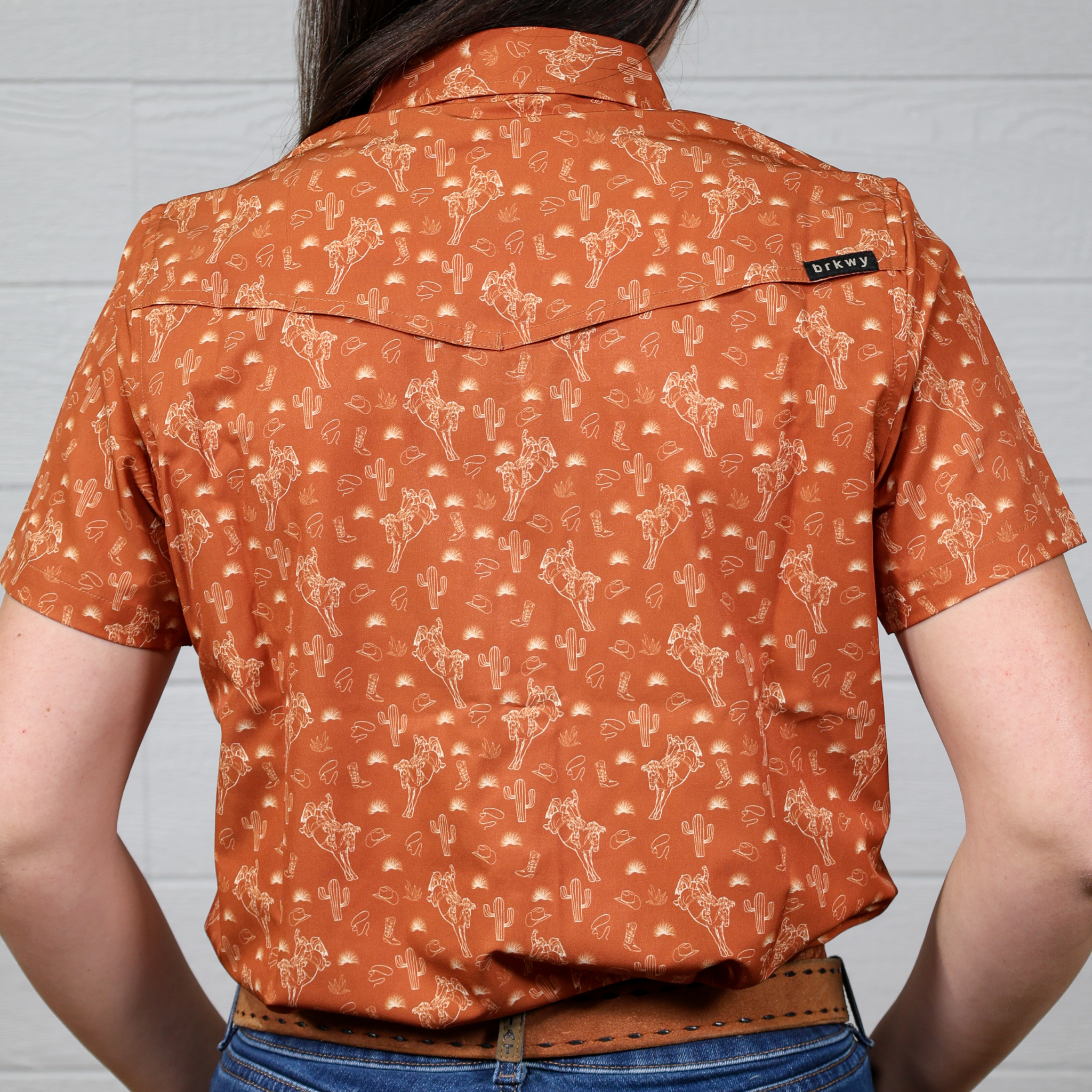Person wearing an orange patterned shirt with a visible brand logo on a White background. Back Facing