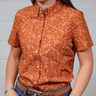 Person wearing a patterned orange shirt with a plain background. forward facing.