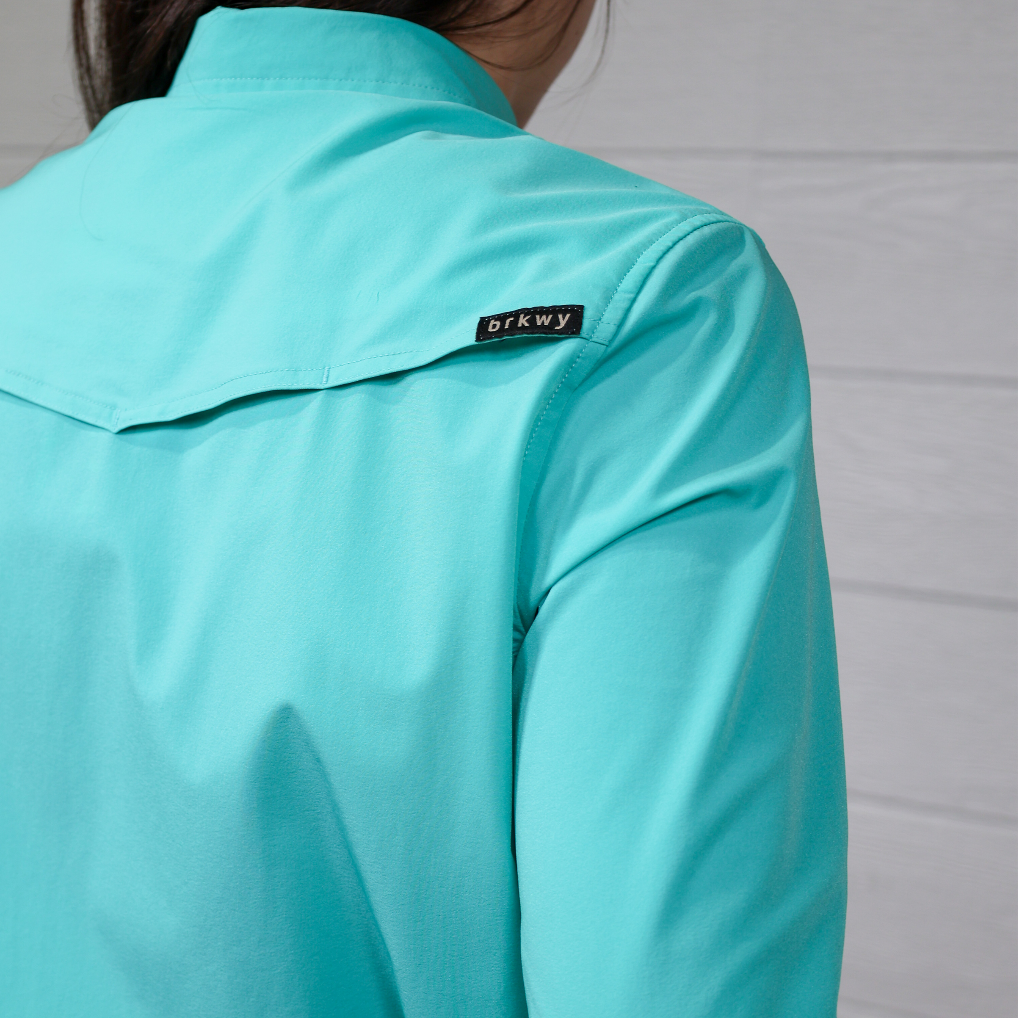 teal button down  with a brand logo on the shoulder against a white background.