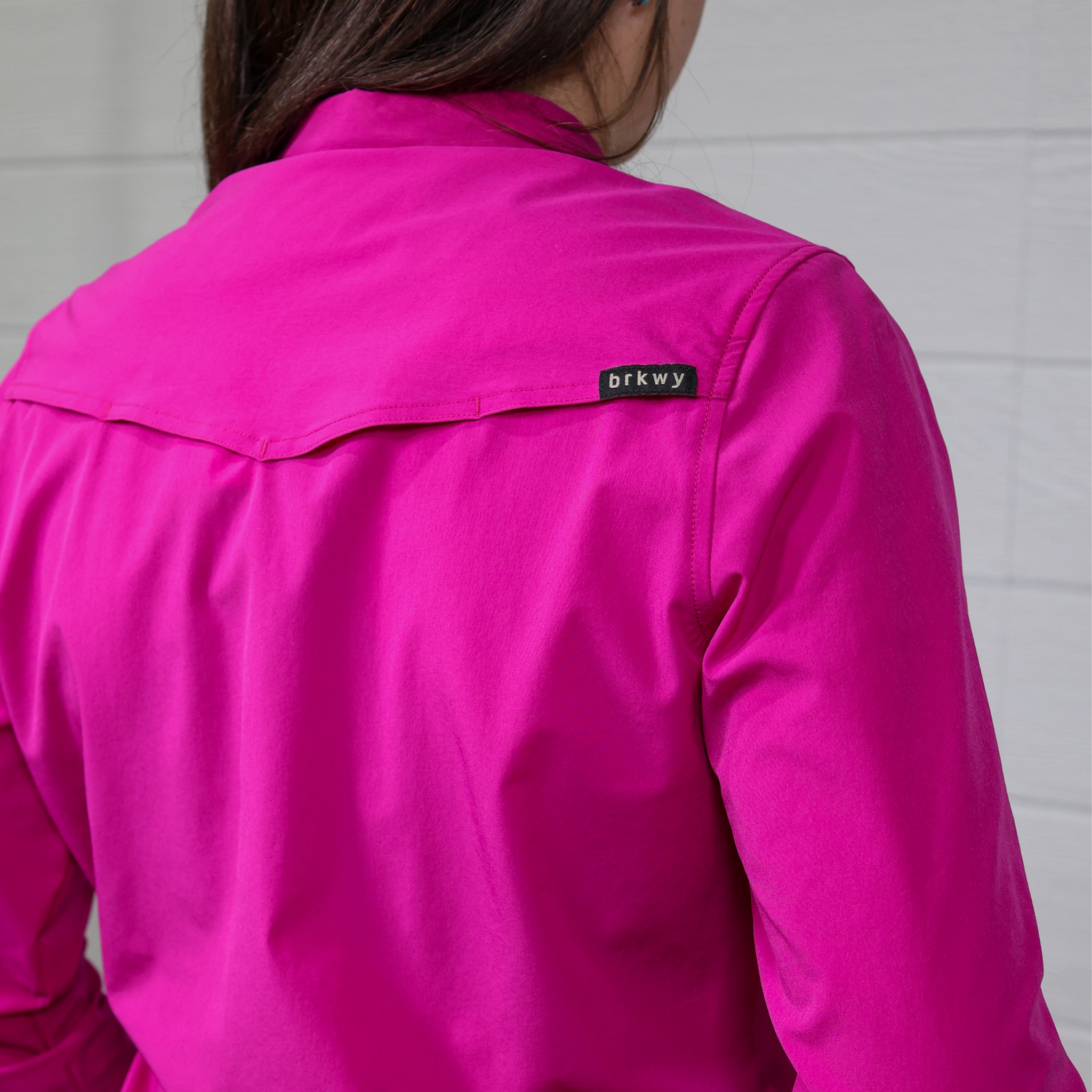 Person wearing a bright pink button down with a brand logo on a white background