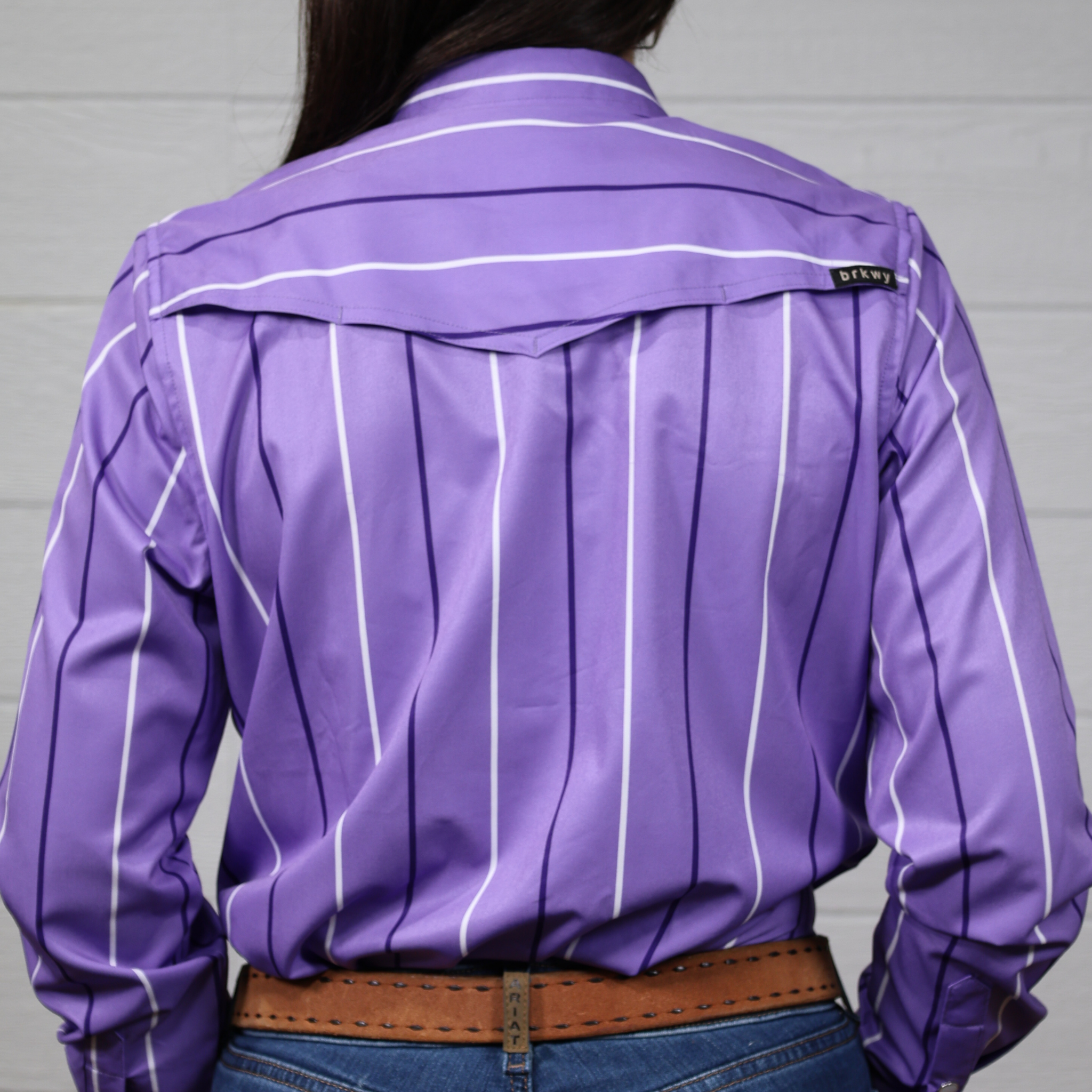 Purple shirt with white stripes worn by a person against a white background. Back facing