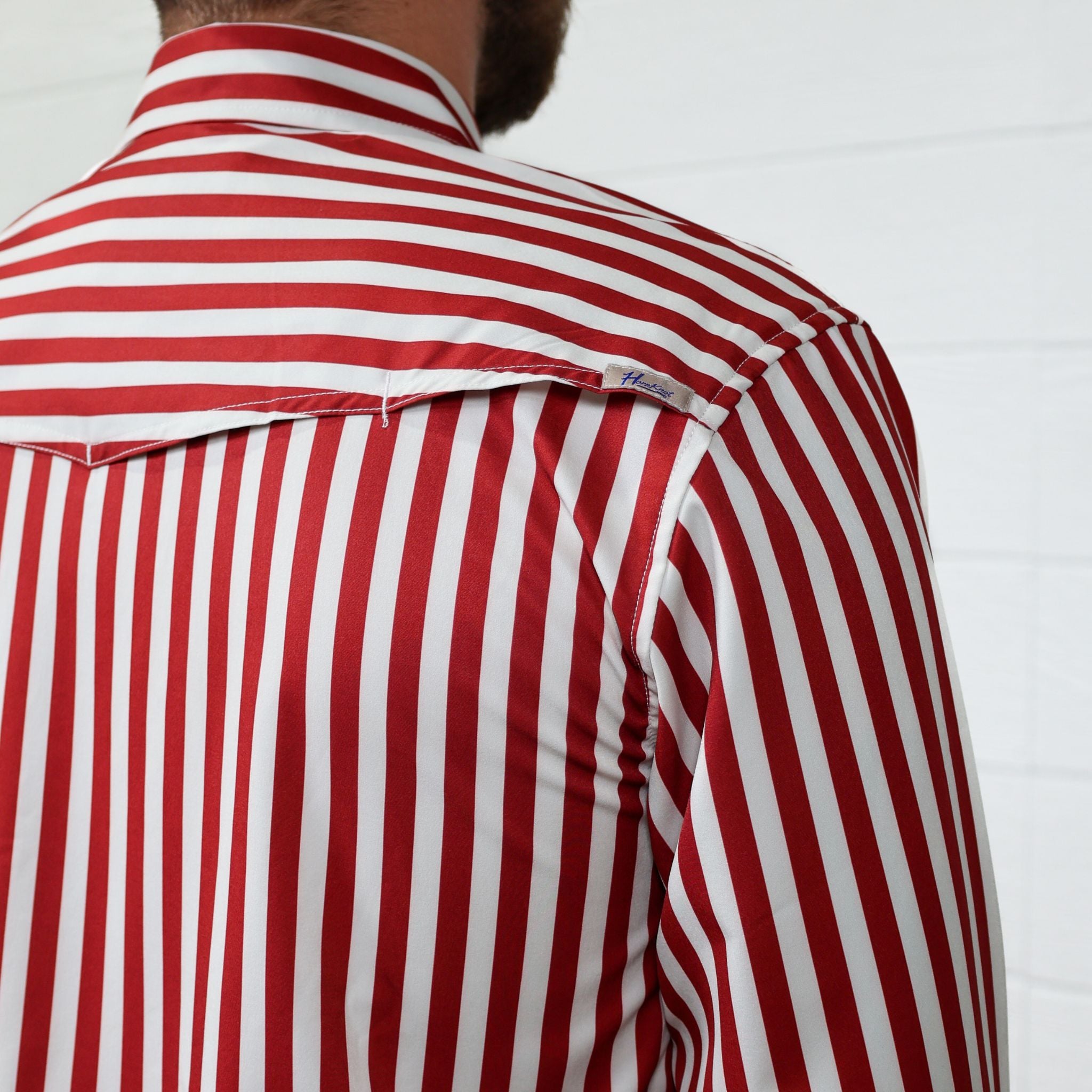 Red and white striped shirt with a brand label on a plain background showing the vent of the shirt