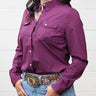 A woman wearing a long-sleeve button-up western shirt in deep purple, tucked into blue jeans with a large western belt and buckle.