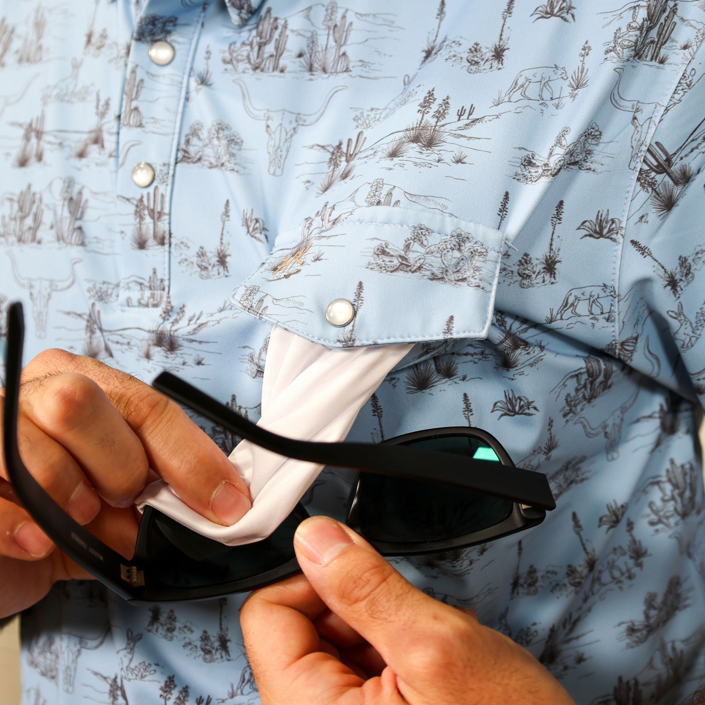 Person sunglasses showing the lens cleaning cloth with a patterned shirt in the background