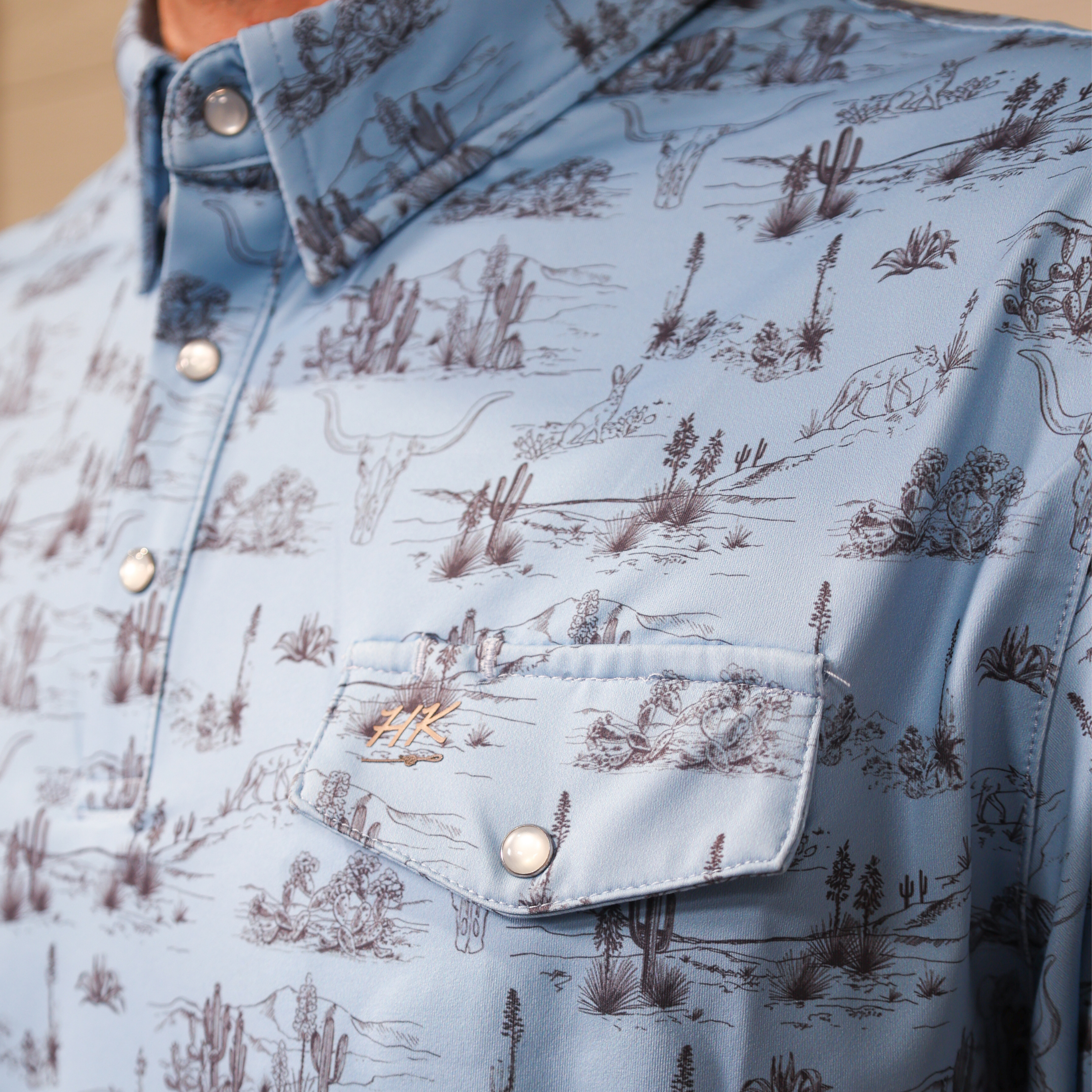 Close-up of a light blue polo with nature-themed print showing the pocket 