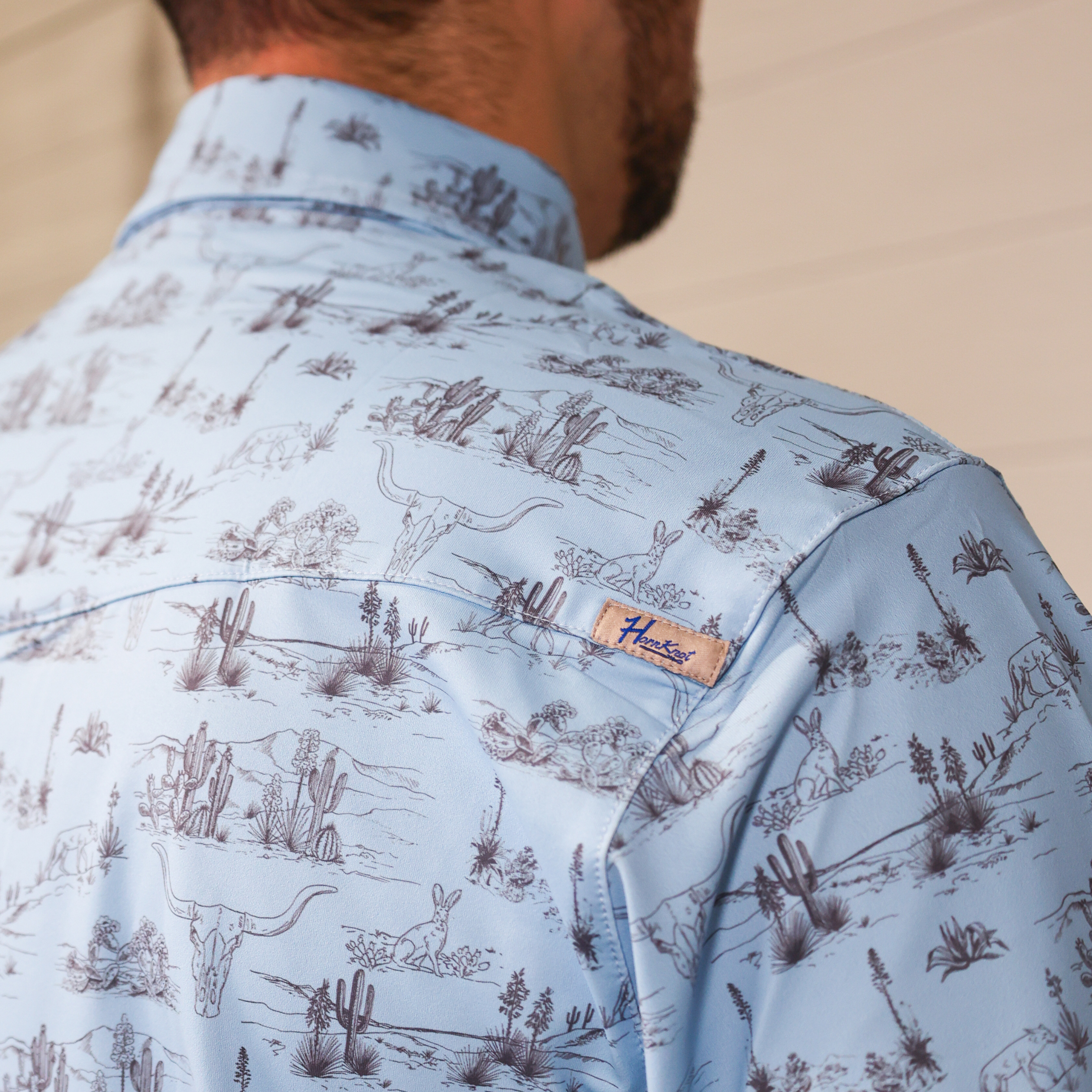 Close-up of a light blue shirt with nature-themed pattern and brand label.