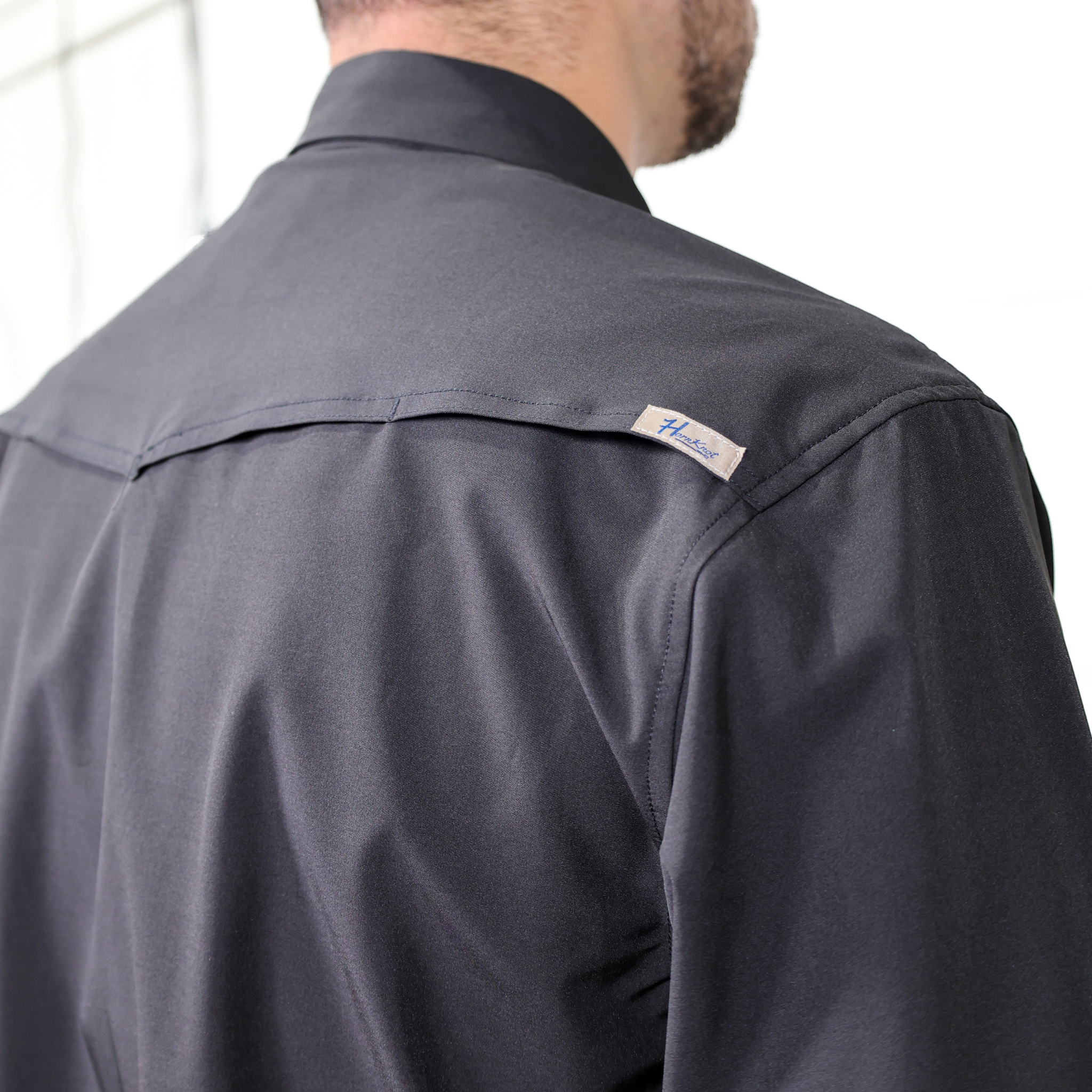 Black shirt with a visible brand logo on the shoulder against a white background. Back Facing