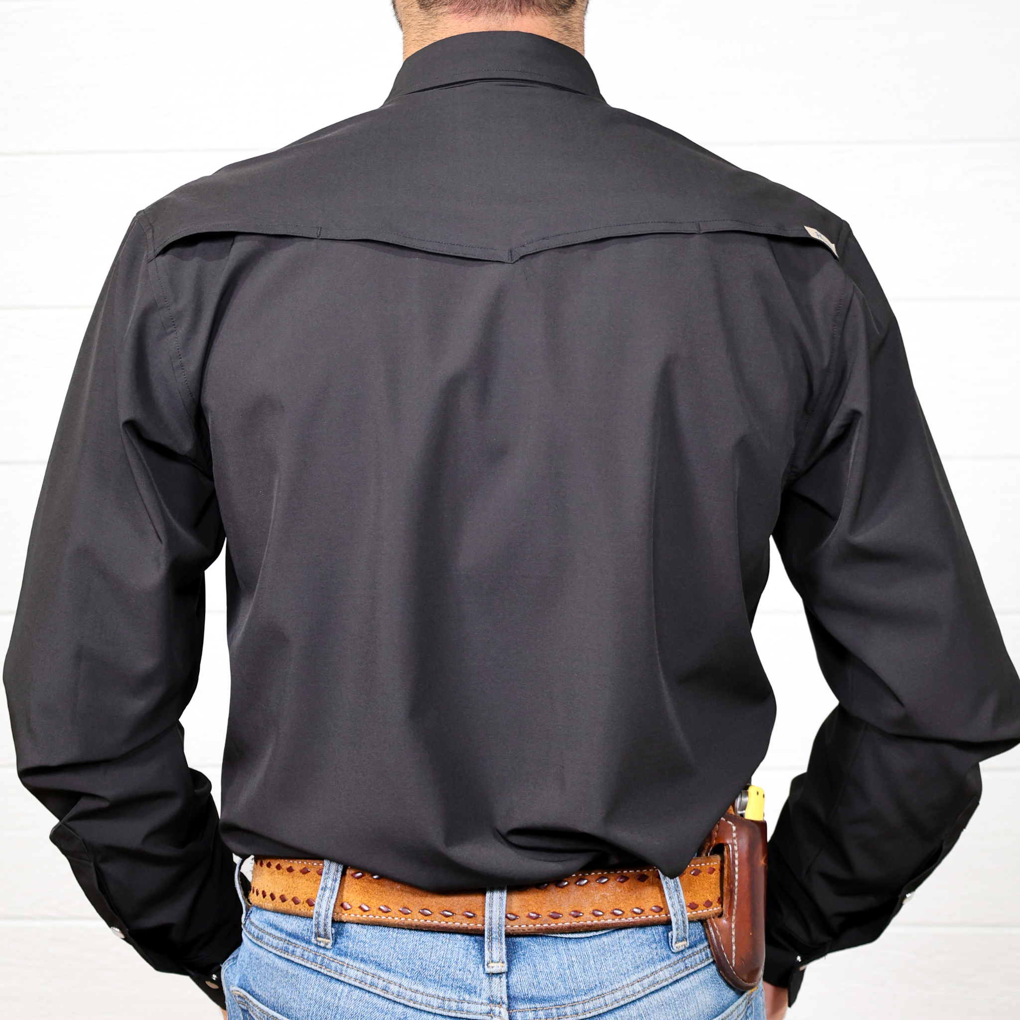 Person wearing a black shirt and blue jeans with a brown belt on a white background. back facing. 