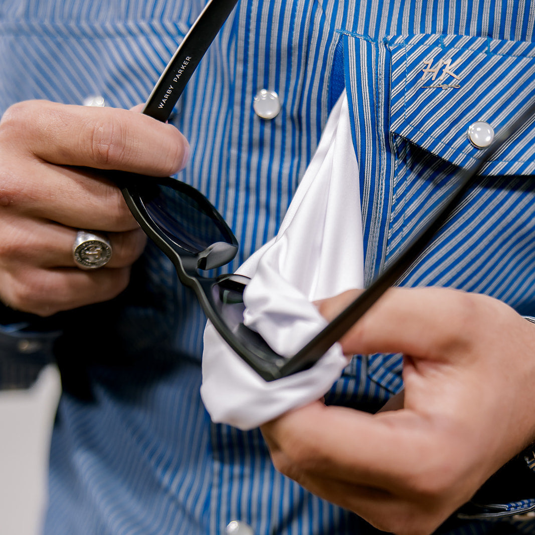 Person cleaning sunglasses with a white cloth against a blue striped shirt background