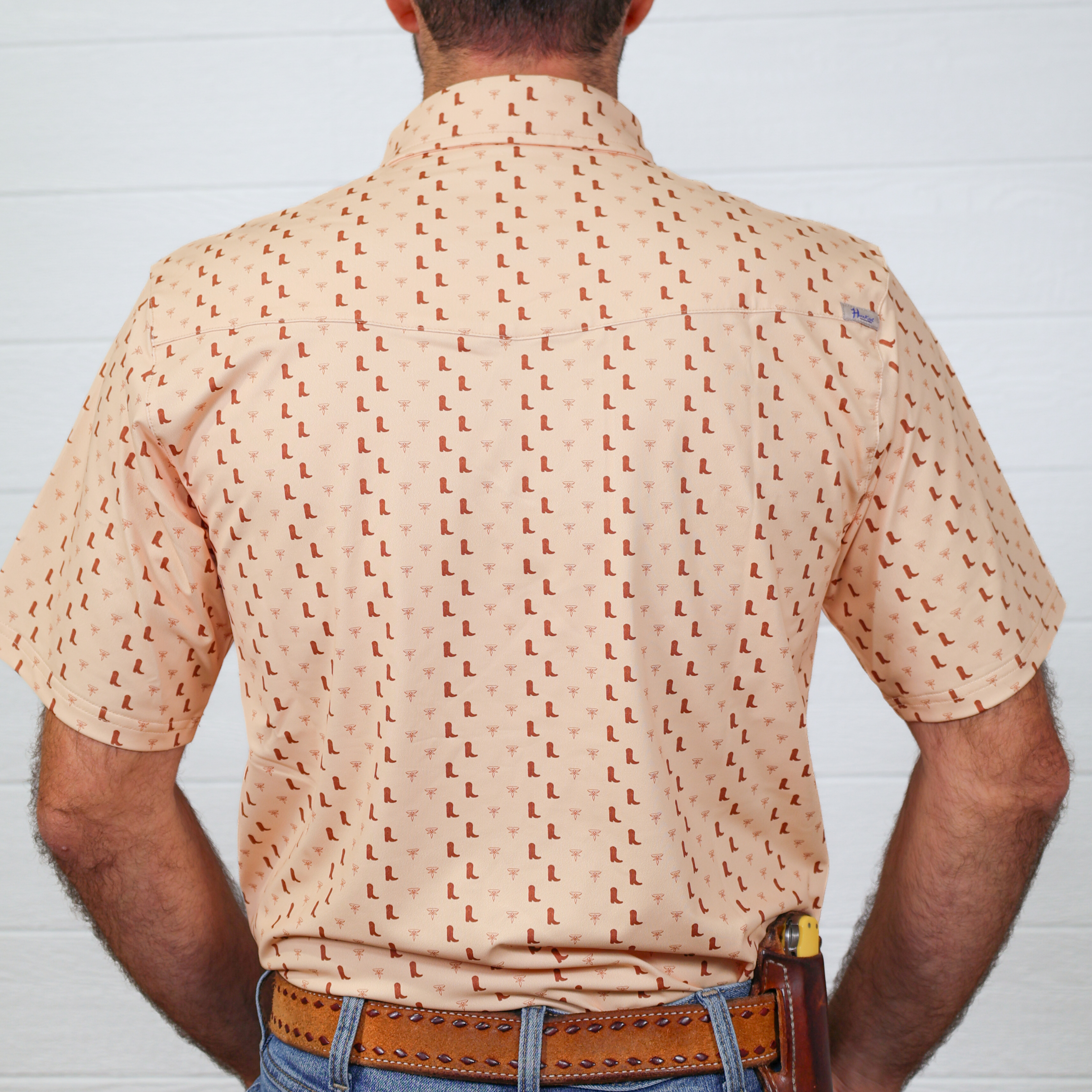 Man wearing a patterned polo with a visible brand logo against a white wall showing the back