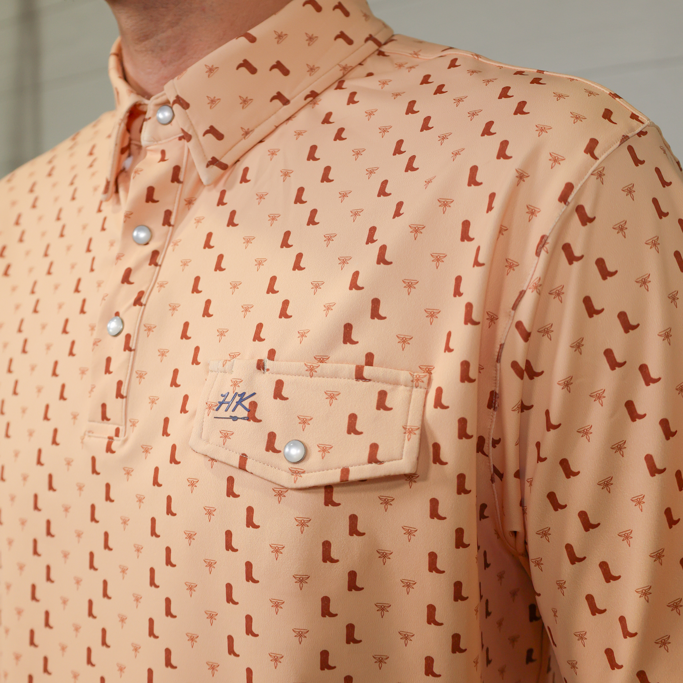 Close-up of a peach-colored shirt with a pattern featuring a pocket with a brand logo.