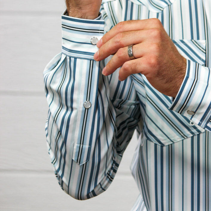 A close-up of a man wearing a blue and white vertically striped dress shirt, adjusting the cuff with one hand while wearing a silver ring with the other.