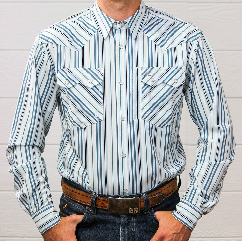 A man wearing a long-sleeve western-style button-up shirt with vertical blue, navy, and white stripes, paired with a brown leather belt and dark blue jeans against a white wood-paneled wall.