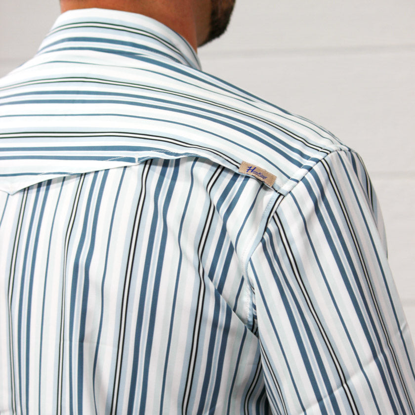 Close-up back view of a man wearing a white long-sleeve button-up shirt with vertical blue and black stripes. A small woven neck label is visible on the shoulder.