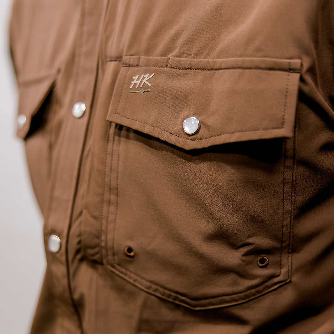 Close-up of a brown shirt with a brand logo on a neutral background