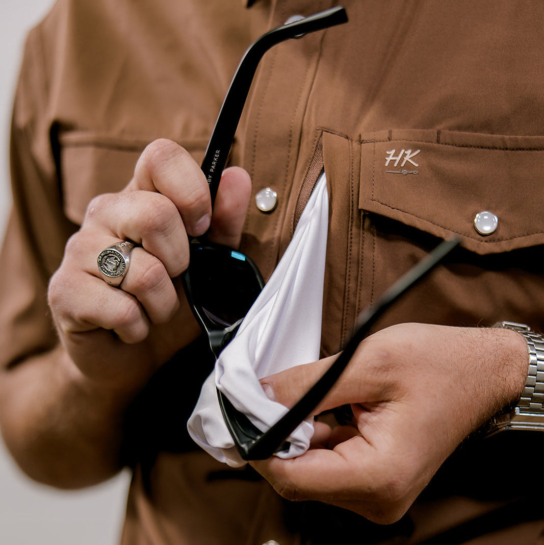 Person holding sunglasses with a brown shirt and blue jeans.