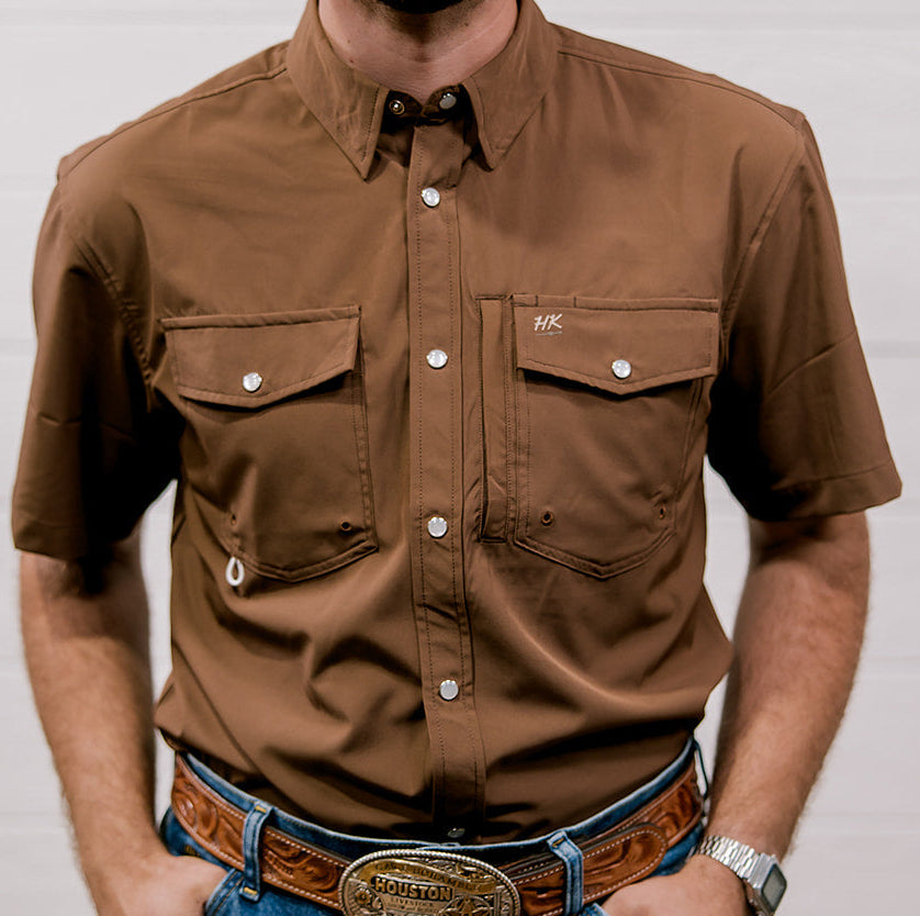 Man wearing a brown shirt and blue jeans with a belt buckle, standing against a plain background. Front Facing
