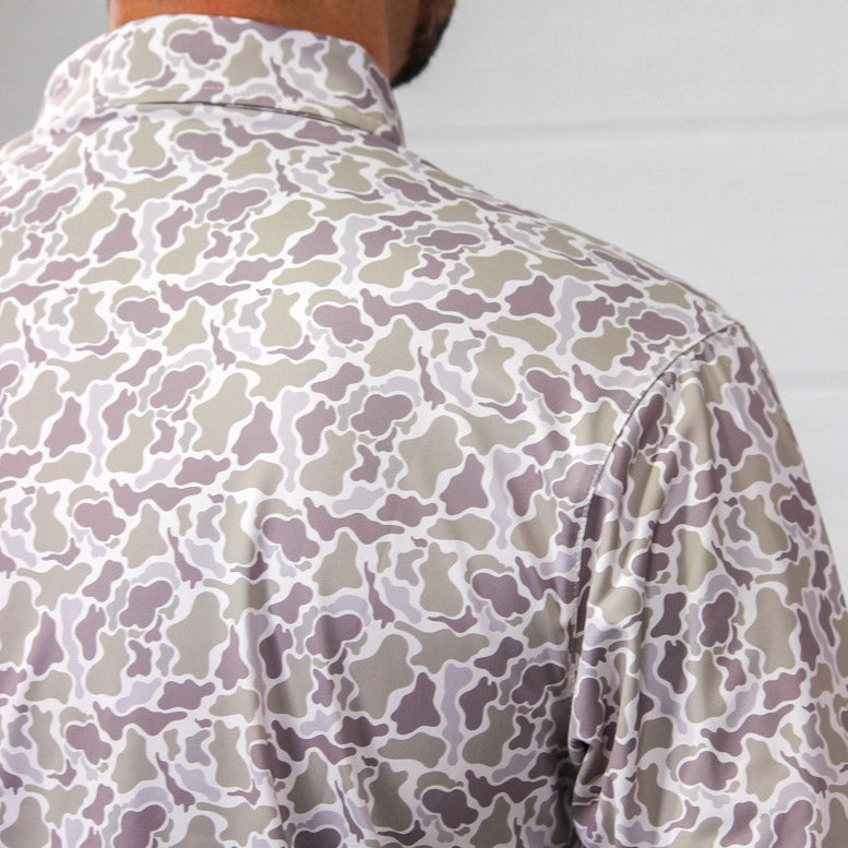 Close-up back view of a person wearing a long-sleeve collared shirt with an abstract organic camouflage pattern in beige, taupe, and muted gray on a white base.