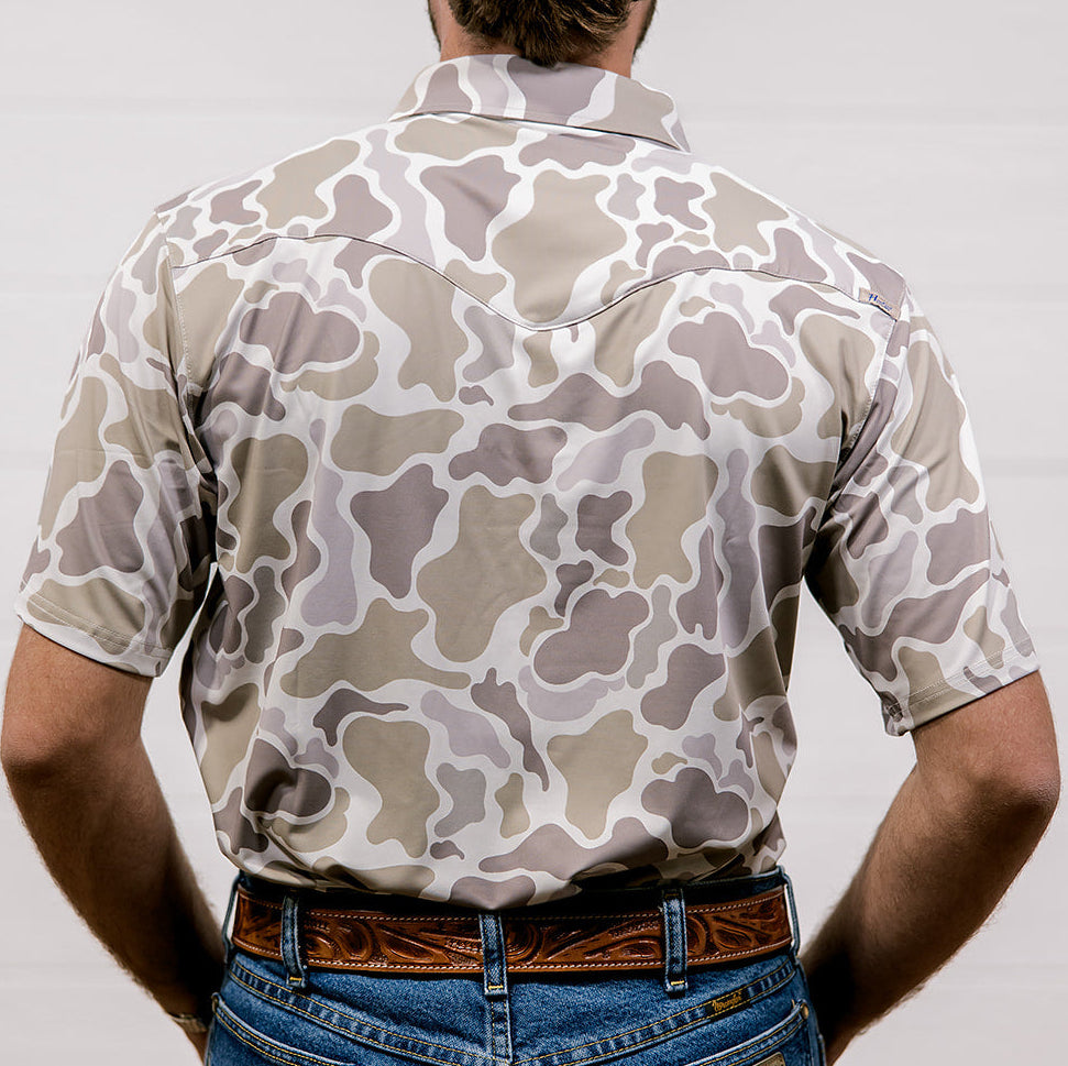 Person wearing a camouflage polo and blue jeans against a plain background. back facing.