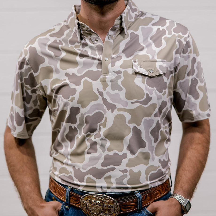 Man wearing a camouflage polo and jeans with a white background. front facing. 