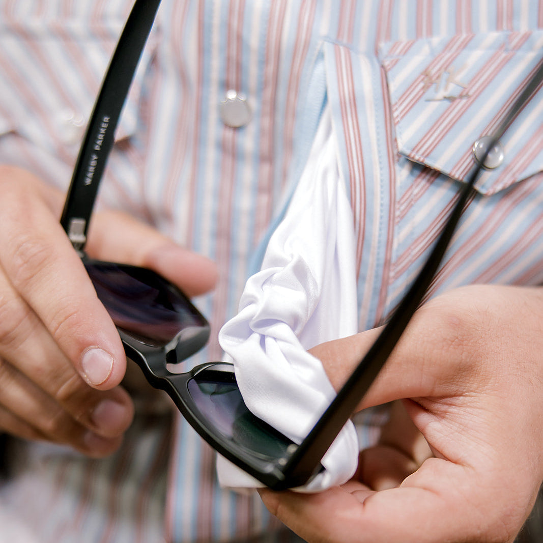 Person cleaning sunglasses with a cloth against a striped shirt background.