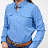 Women wearing a denim blue pearl snap long sleeve top tucked in to blue jeans with a belt in front of a white wall. 