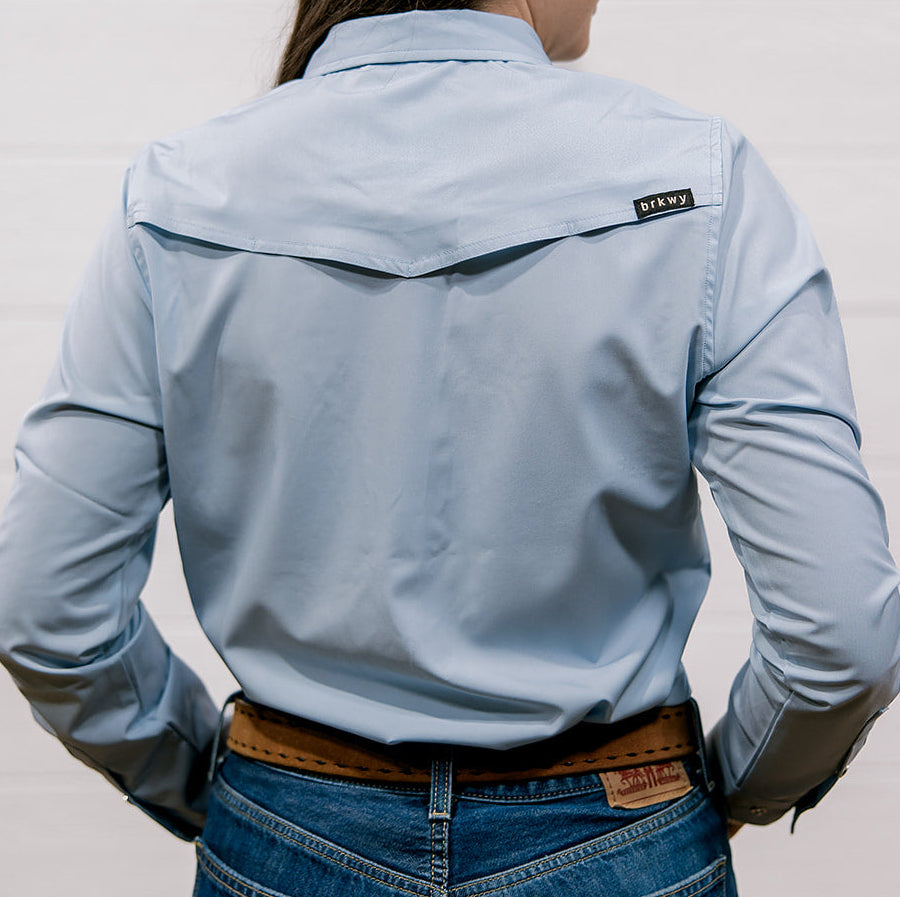 Person wearing a light blue shirt with a visible brand logo against a white background showing the back 