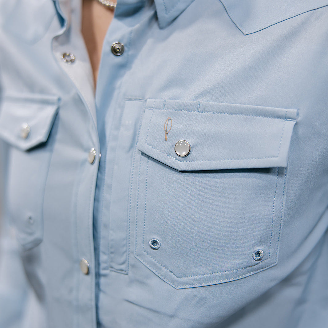 Light blue denim shirt with button details on a neutral background showing the slanted pocket 