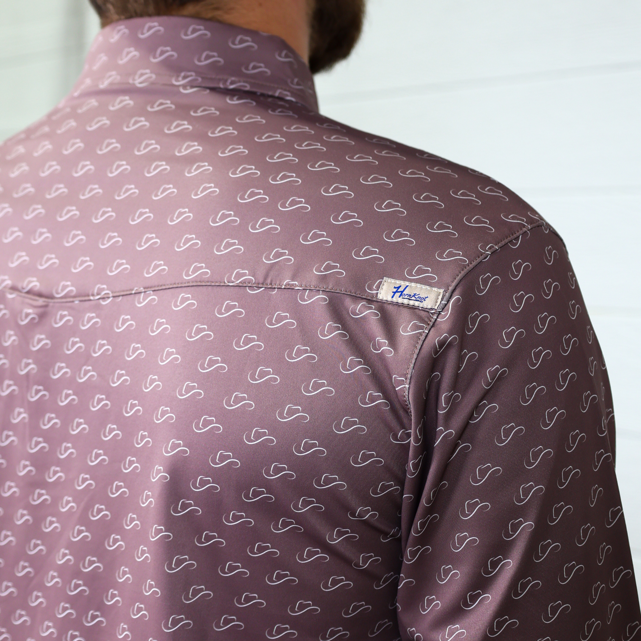 Close-up of a brown patterned polo with a visible brand labe on the vent and  a white background