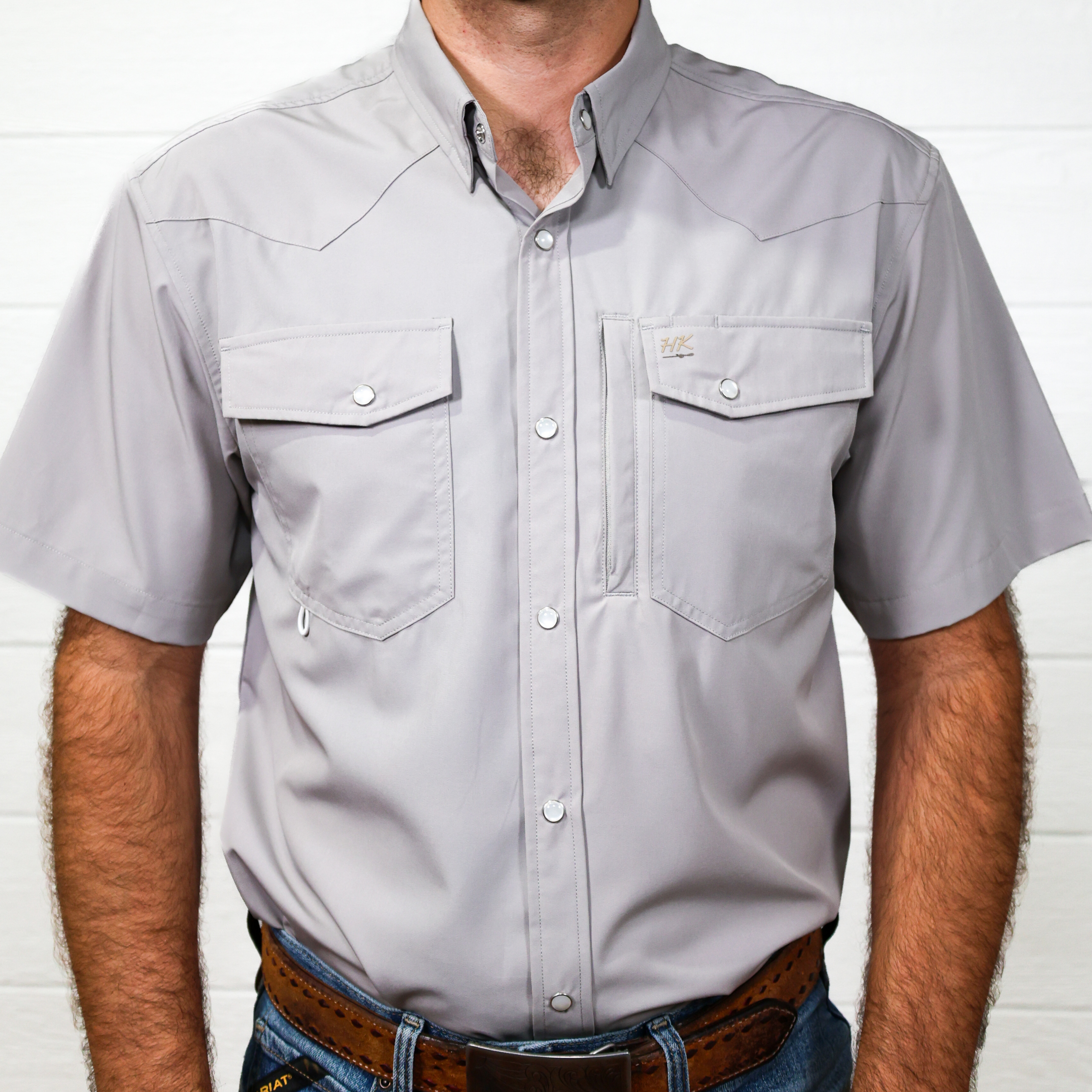 Man wearing a gray short-sleeve shirt with two front pockets against a white background showing the front 