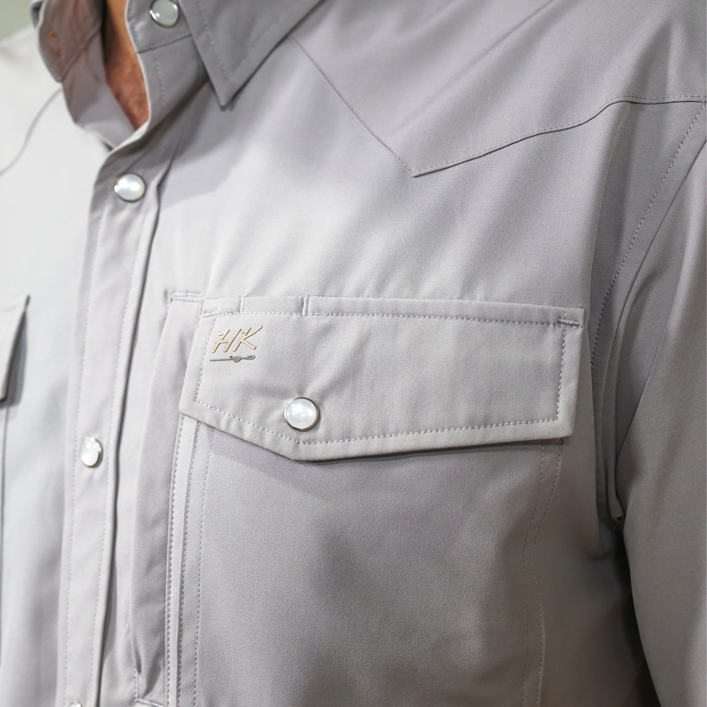 Close-up of a gray shirt with a brand logo on the chest pocket.