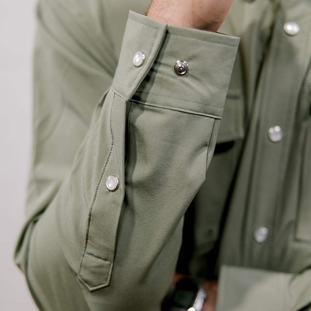 Close-up of a person wearing a green shirt with button details on a plain background