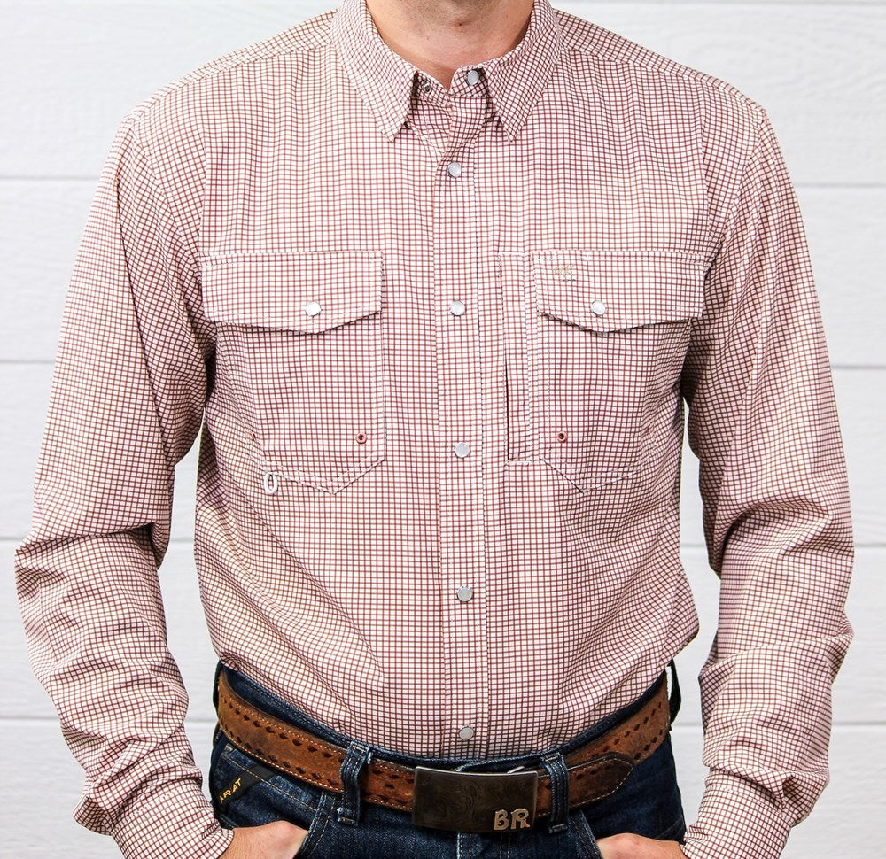 A man wearing a long-sleeve button-down western shirt with a fine red and white gingham pattern, paired with a brown leather belt and dark blue jeans against a white wood-paneled wall.
