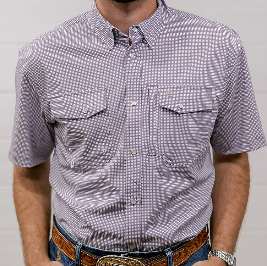 Man wearing a light purple checkered shirt and blue jeans with a belt buckle, standing against a white wall. front facing. 