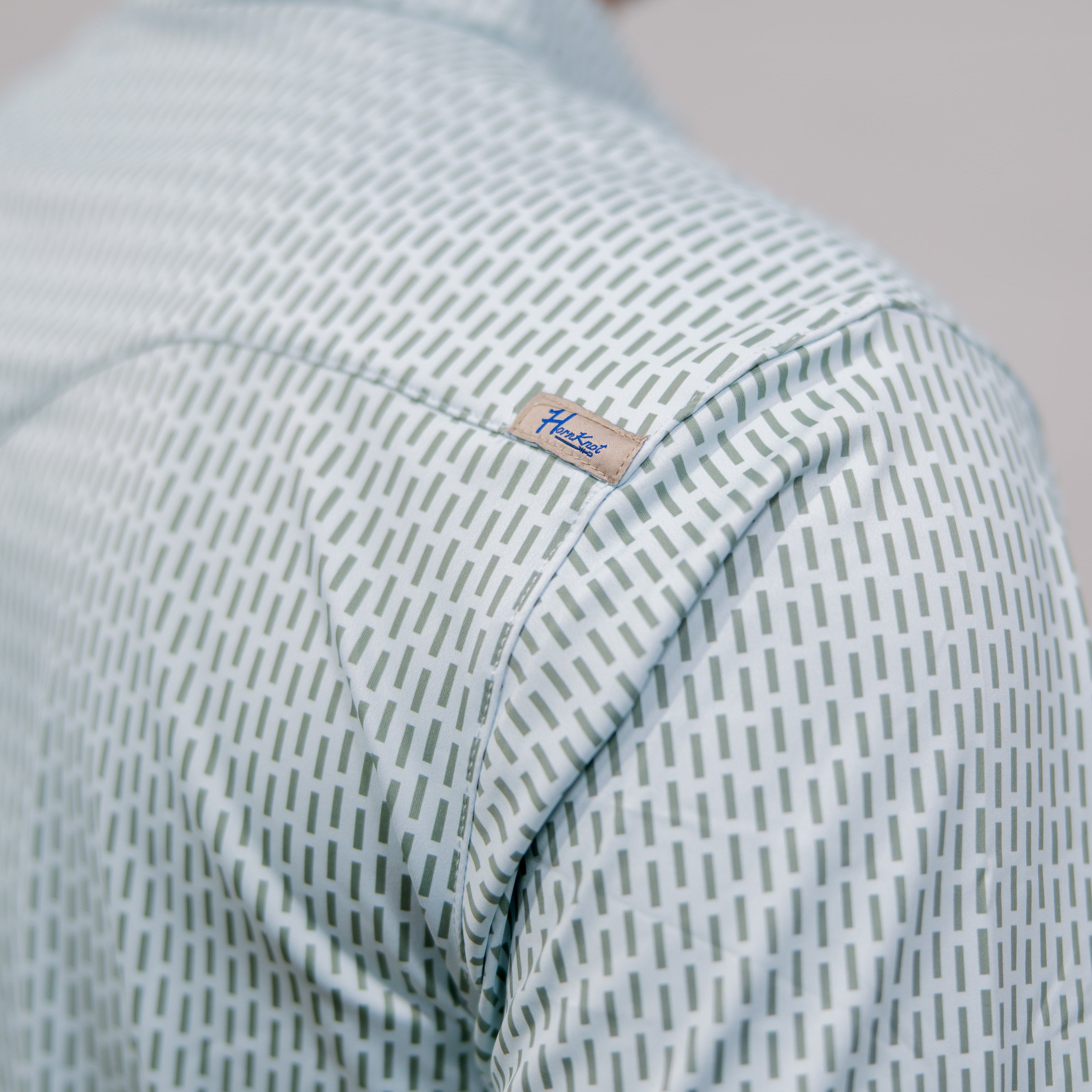 Close-up of a person wearing a light blue and green patterned shirt with a brand label on the back yoke. 