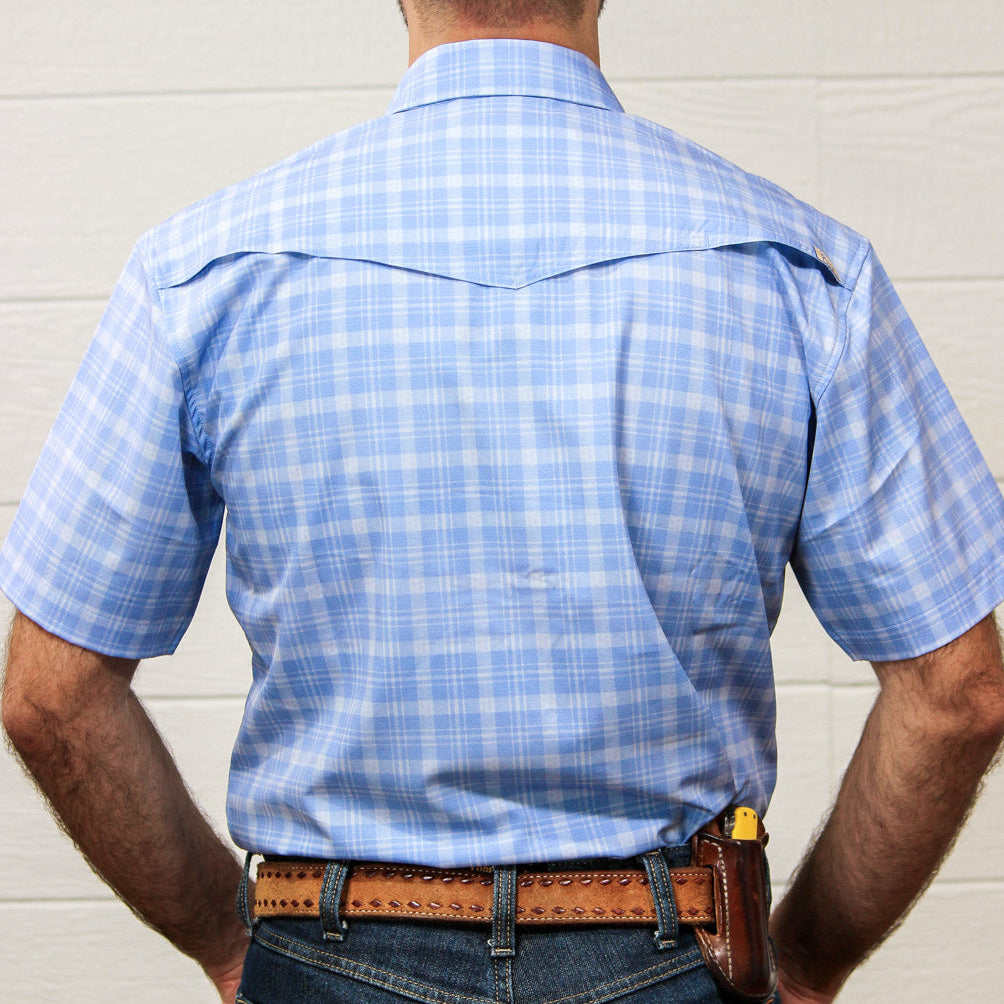 A man viewed from behind wearing a light blue and white plaid short-sleeve western shirt, blue jeans, and a brown leather belt with a holster.