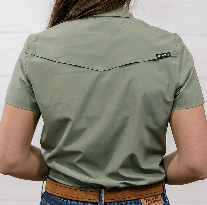 Person wearing a Sage green shirt and blue jeans against a white background showing the back 