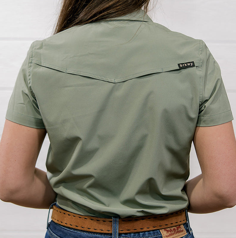 Person wearing a Sage green shirt and blue jeans against a white background showing the back 