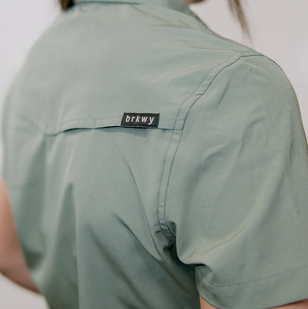 Person wearing a sage green shirt with a brand label 'brkwy' on a plain background