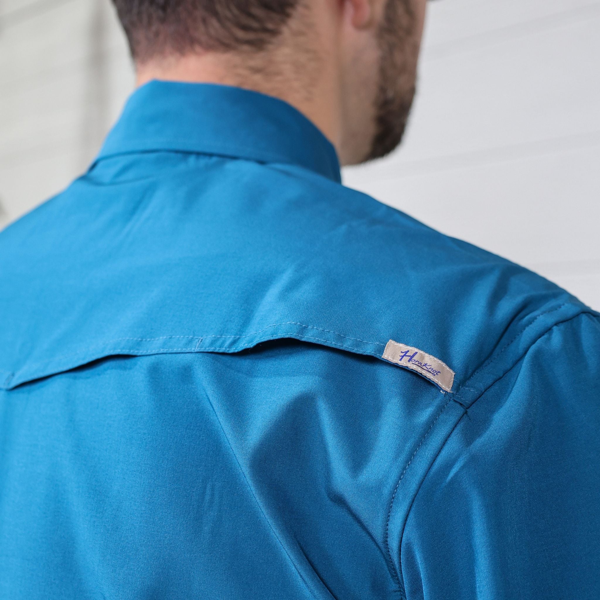 Close-up of a blue shirt with a brand label on the sleeve against a white background showing the vent 