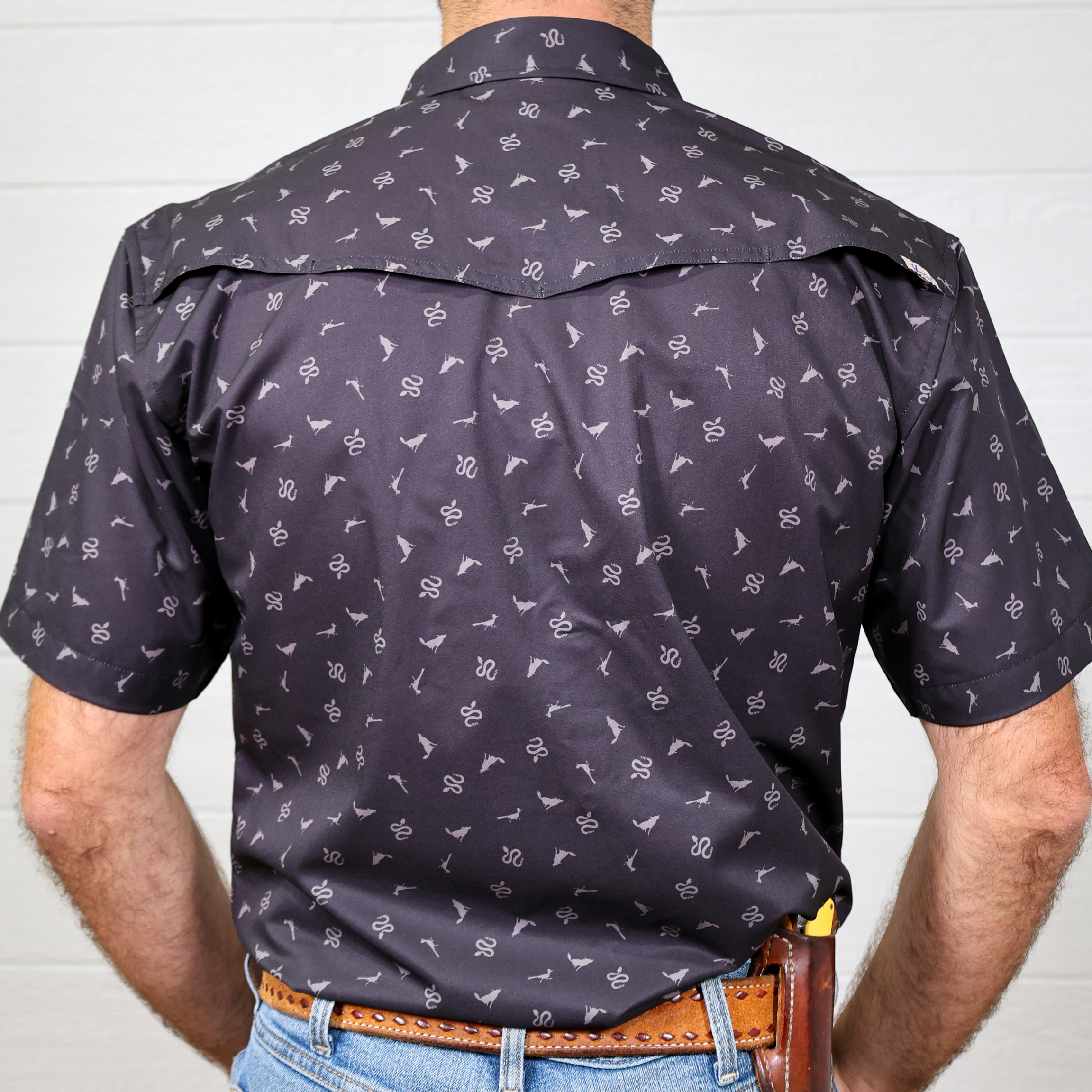 Man wearing a dark patterned shirt with a white background showing the back 