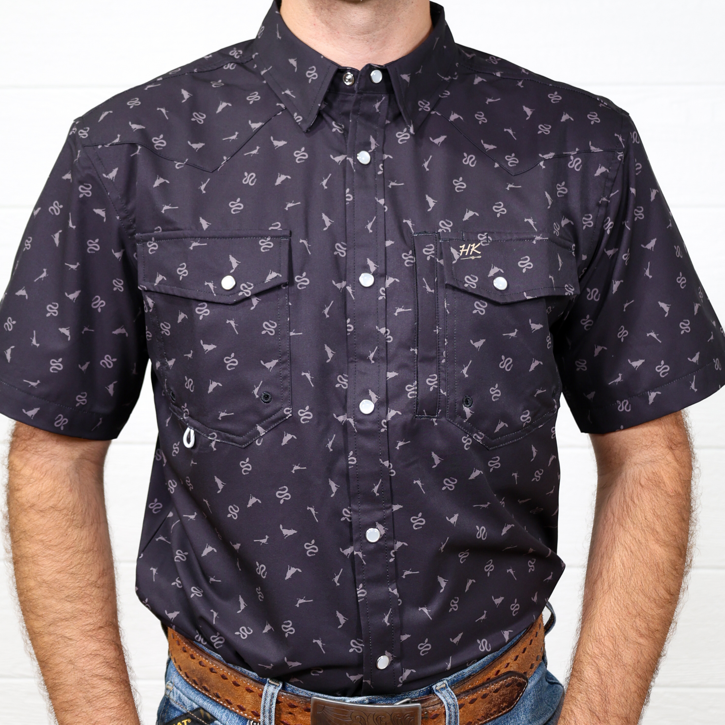 black short-sleeve shirt with white pattern worn by a person against a white brick wall showing the front.