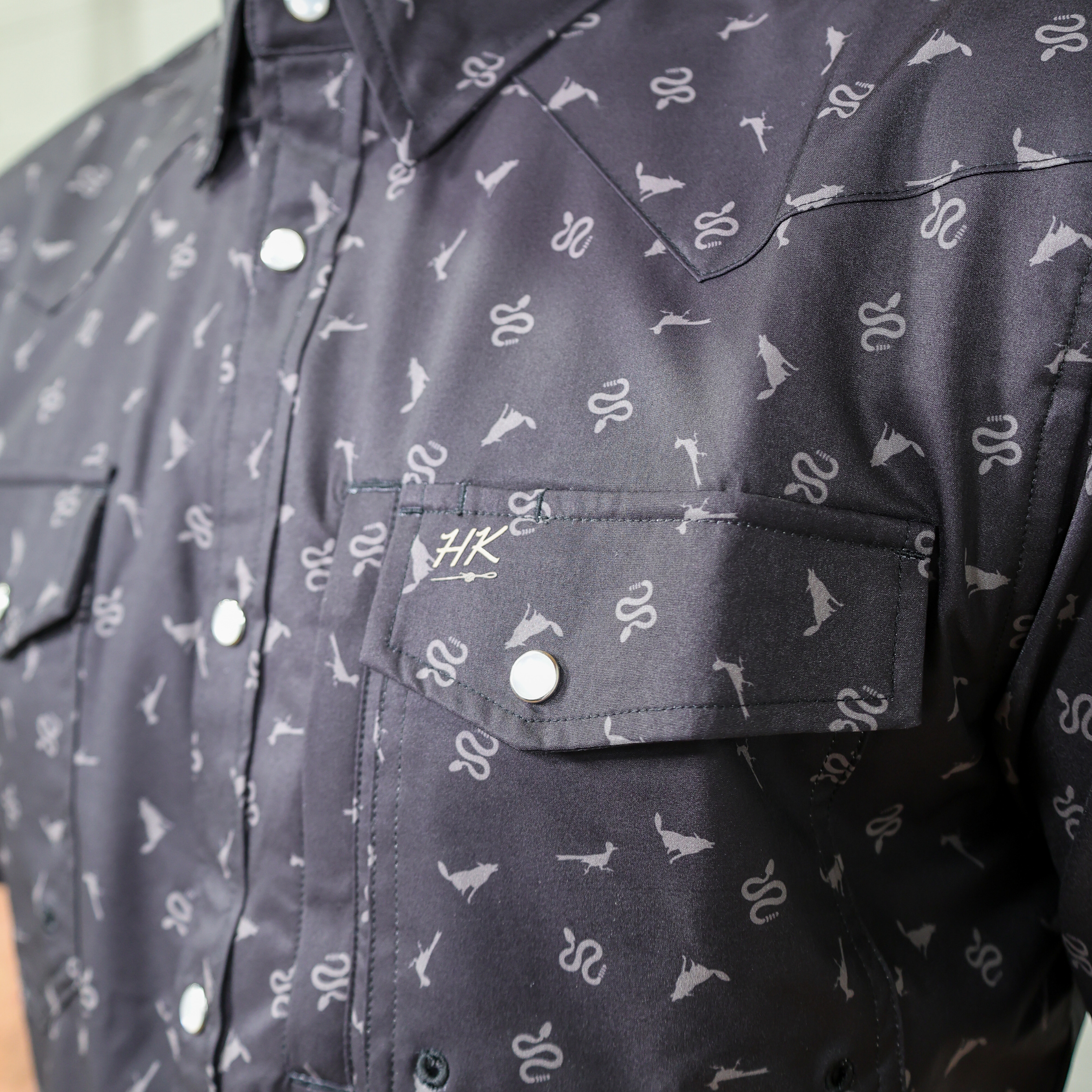 Close-up of a black shirt with white pattern and brand logo showing the pocket